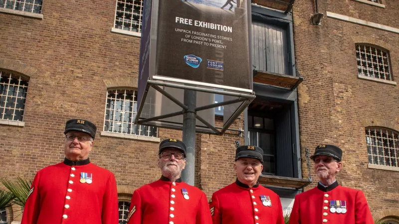 Chelsea Pensioners stood outside Museum of London Docklands and sign for PLA exhibition London: Port City
