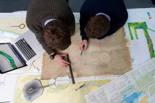 People leaning over maps of the River Thames and a laptop Hydrography team